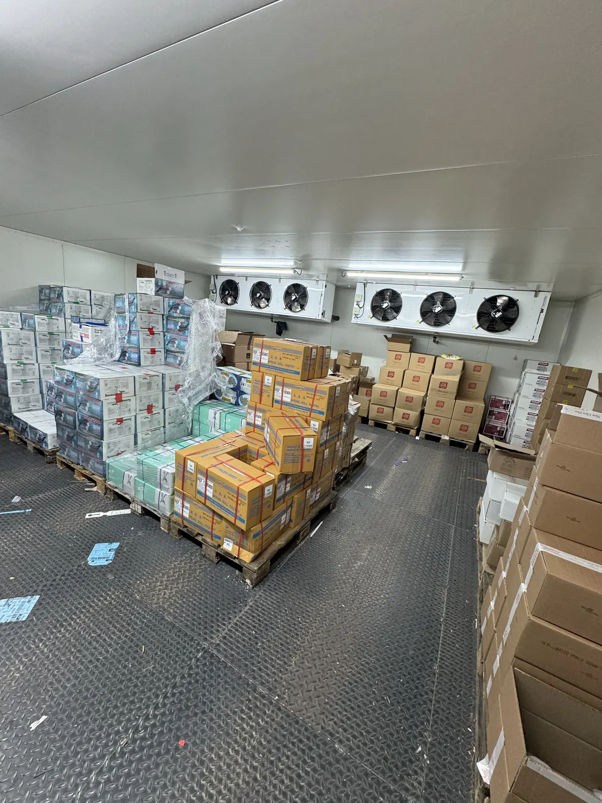 Grand entrepôt frigorifique avec plusieurs évaporateurs au plafond et des palettes de marchandises.