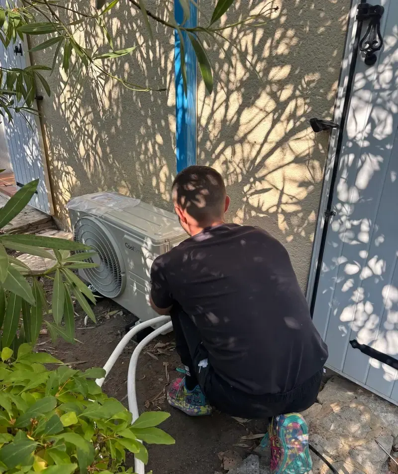 Technicien LCDH13 raccordant une unité extérieure de climatisation le long d'un mur de maison.